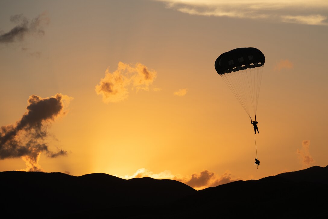 A soldier parachutes to the ground at twilight.