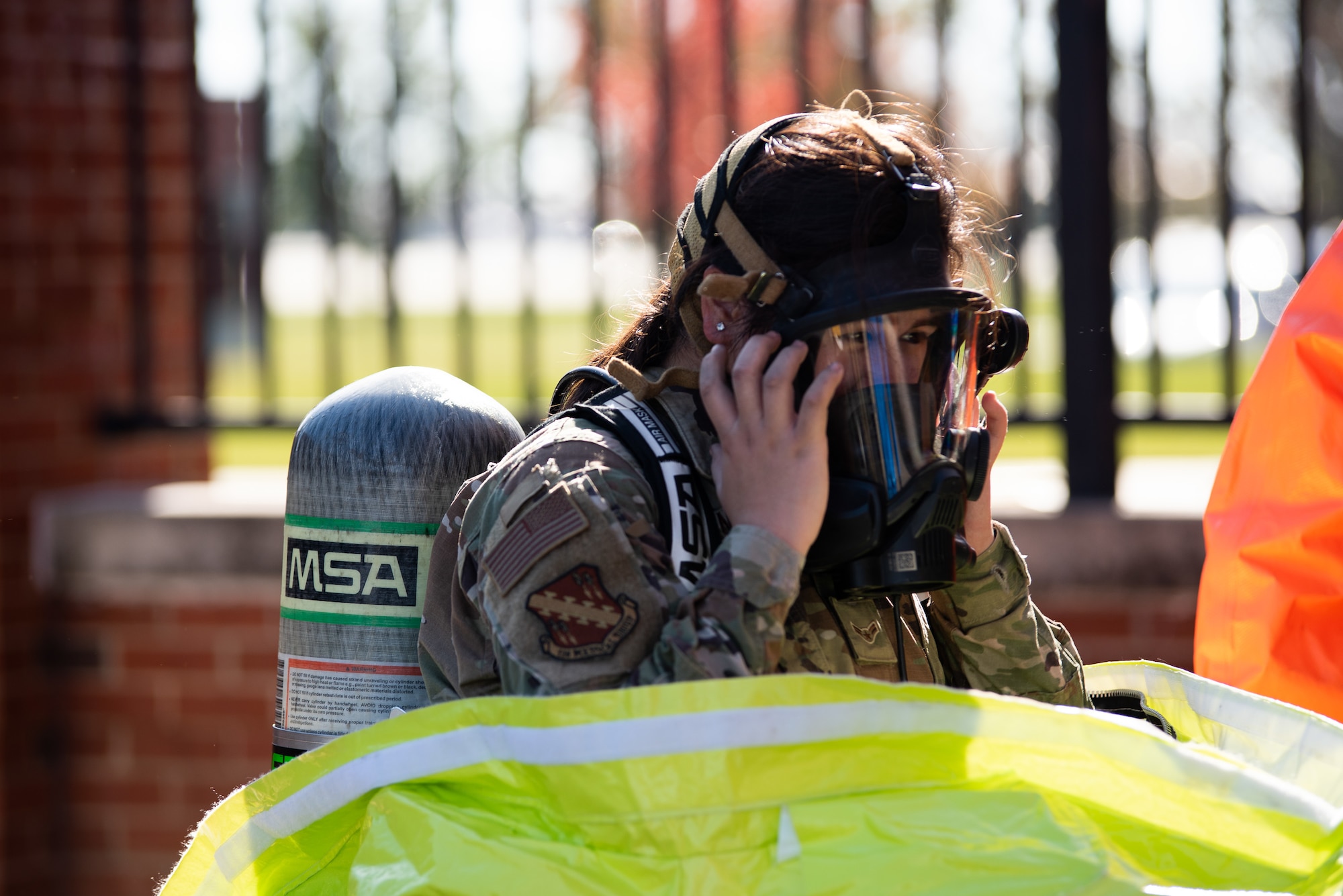 An airman puts on the self-contained breathing apparatus that covers her entire face. She has an oxygen tank on her back