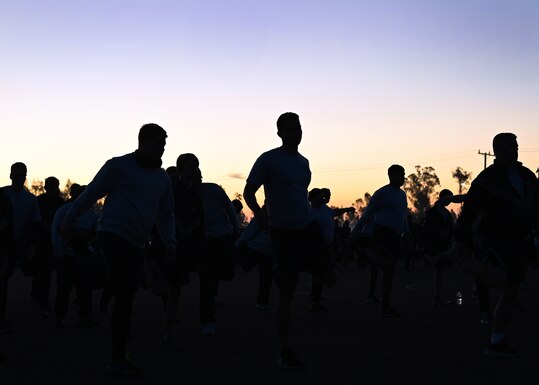 Silhouette of Airmen and Guardians doing group stretches