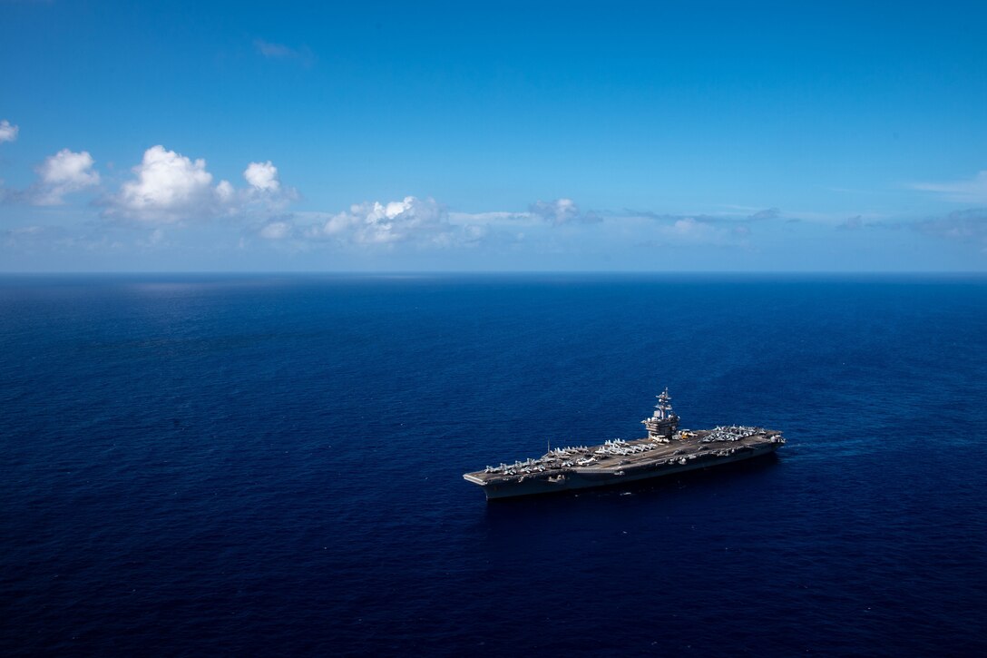 An aircraft carrier moves across dark blue water.