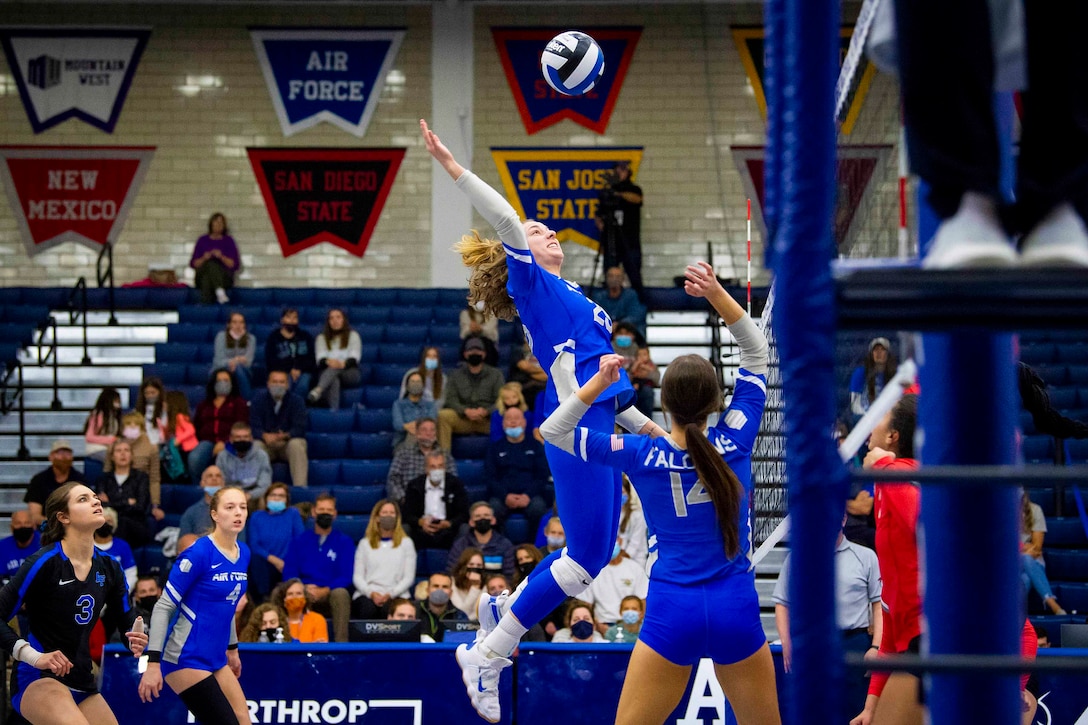 An Air Force cadet jumps to hit a volleyball over a net as other watch.