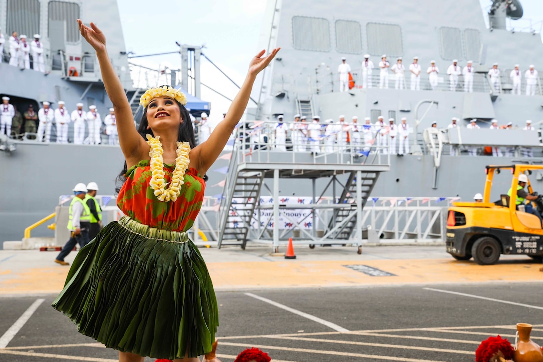 A woman dances in front of a ship as sailors exit.