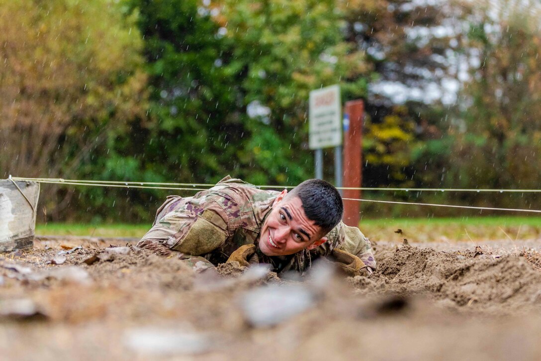 A soldier crawls underneath wire.