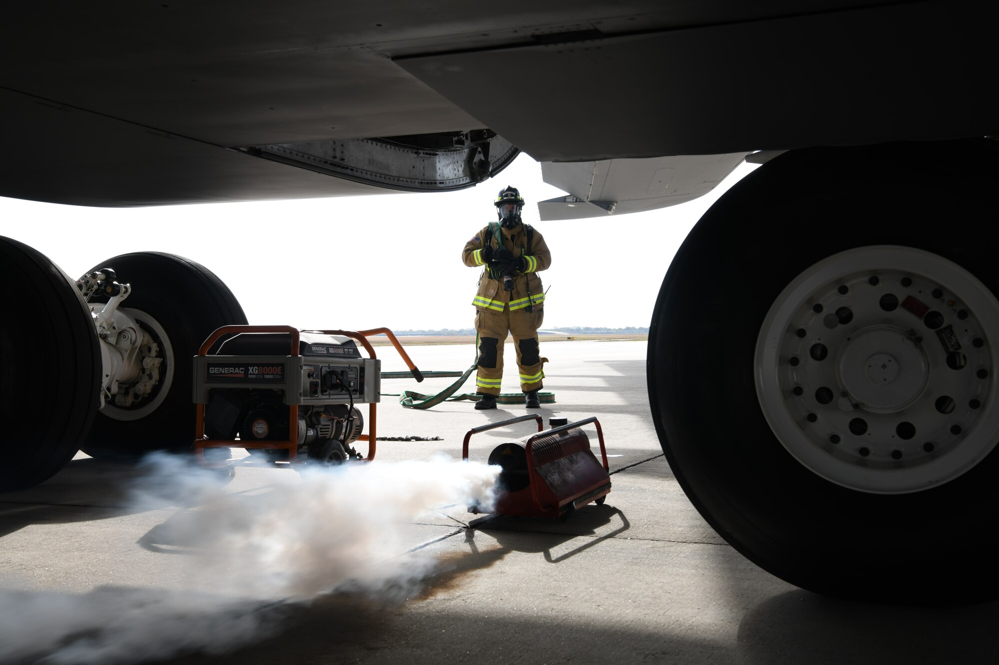 A 902nd Civil Engineer Squadron firefighter, gets into position to fight a simulated brake fire on a C-5M Super Galaxy cargo aircraft during a total force exercise Nov. 15, 2021, at Joint Base San Antonio-Lackland, Texas. A smoke machine was used to create a more realistic environment during the training scenario. (U.S. Air Force photo by Master Sgt. Kristian Carter)