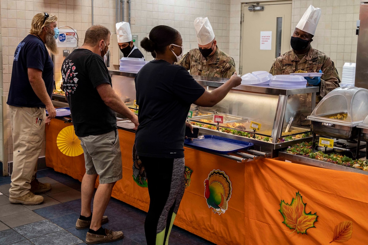 Soldiers serve food to people standing in line at a buffet.