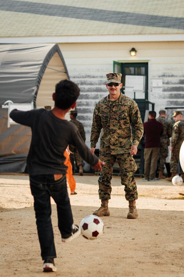 A U.S. Marine with 1st Battalion, 23rd Marine Regiment, plays soccer with an Afghan child on Fort Pickett, Virginia, Nov. 17, 2021. Marines and Sailors of 1/23 recently replaced 3rd Battalion, 6th Marine Regiment and began to build bonds with Afghan individuals awaiting the next steps in their resettlement process. The Department of Defense, through U.S. Northern Command, and in support of the Department of Homeland Security, is providing transportation, temporary housing, medical screening, and general support for at least 50,000 Afghan evacuees at suitable facilities, in permanent or temporary structures, as quickly as possible. This initiative provides Afghan personnel essential support at secure locations outside Afghanistan. (U.S. Marine Corps Lance Cpl. Zachary Zephir)
