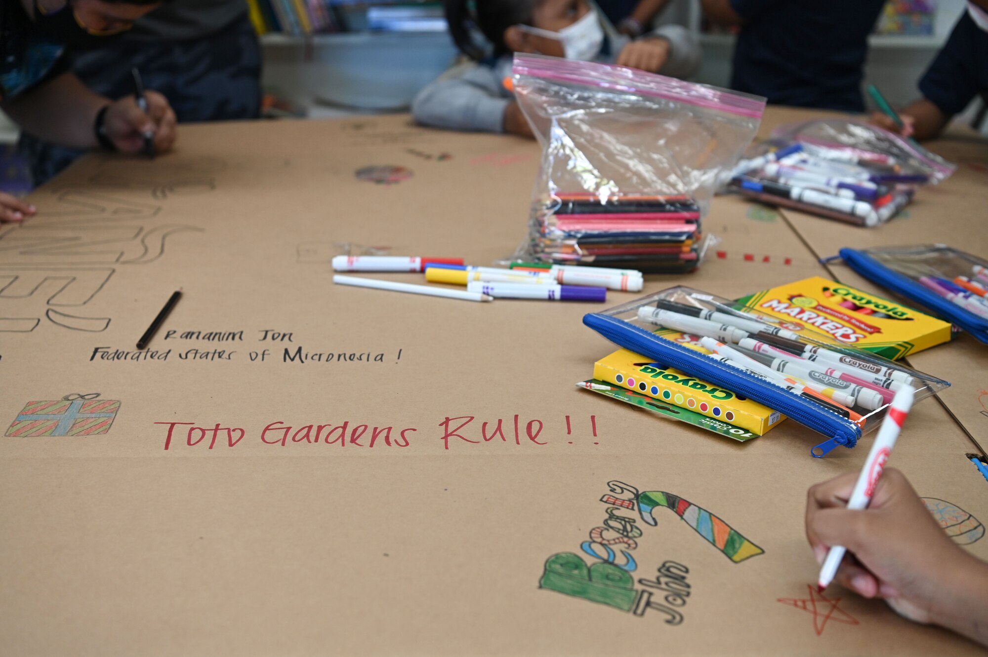 Children with Mañe'lu and Airmen from Andersen Air Force Base, Guam, draw and write messages on a box during a volunteer event at Toto Garden, Mongmong-Toto-Maite, Nov. 18th, 2021. The two Airmen from 36 CPTS volunteered through Andersen Air Force Base’s Sister Village Sister Squadron program and joined the children with Mañe'lu to decorate boxes that will be used during Operation Christmas Drop with donated supplies. (U.S. Air Force photo by Senior Airman Aubree Owens)