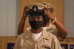 211119-N-GW139-1081 NAVAL SUPPORT ACTIVITY NAPLES, Italy (Nov. 19, 2021) Chief Logistics Specialist Kokou Gbekou, center, dons his cover during a Chief Petty Officer pinning ceremony onboard U.S. Naval Support Activity Naples (NSA), Nov. 19, 2021. NSA Naples is an operational ashore base that enable U.S., allied, and partner nation forces to be where they are needed, when they are needed to ensure security and stability in Europe, Africa, and Southwest Asia. (U.S. Navy Photo by Mass Communication Specialist 1st Class Eric Coffer)
