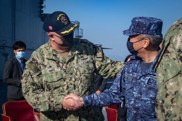 Capt. Ken Ward, left, commanding officer of the forward-deployed amphibious assault ship USS America (LHA 6), shakes hands with Japan Maritime Self-Defense Force Rear Adm. Takuhiro Hiragi, commander, Fleet Air Wing 31, on the ship’s flight deck during a port visit to Marine Corps Air Station Iwakuni. America, lead ship of the America Amphibious Ready Group, is operating in the U.S. 7th Fleet area of responsibility to enhance interoperability with allies and partners and serve as a ready response force to defend peace and stability in the Indo-Pacific region.