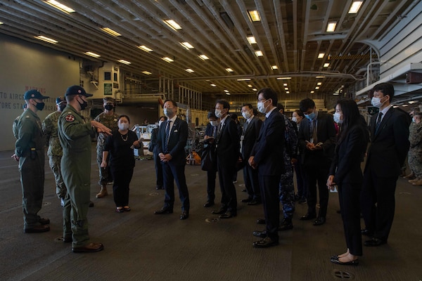 Lt. Alex Castillo, foreground left, the hangar deck officer aboard the forward-deployed amphibious assault ship USS America (LHA 6), conducts a tour of the ship’s hangar for local and regional civic and military leadership during a port visit to Marine Corps Air Station Iwakuni. America, lead ship of the America Amphibious Ready Group, is operating in the U.S. 7th Fleet area of responsibility to enhance interoperability with allies and partners and serve as a ready response force to defend peace and stability in the Indo-Pacific region.