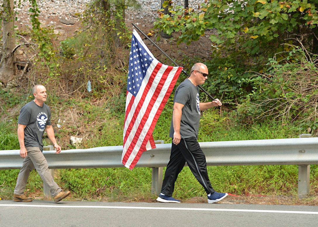 Two veterans walk down the side of the road holding an American flag.