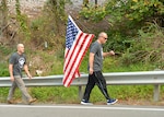 Two veterans walk down the side of the road holding an American flag.