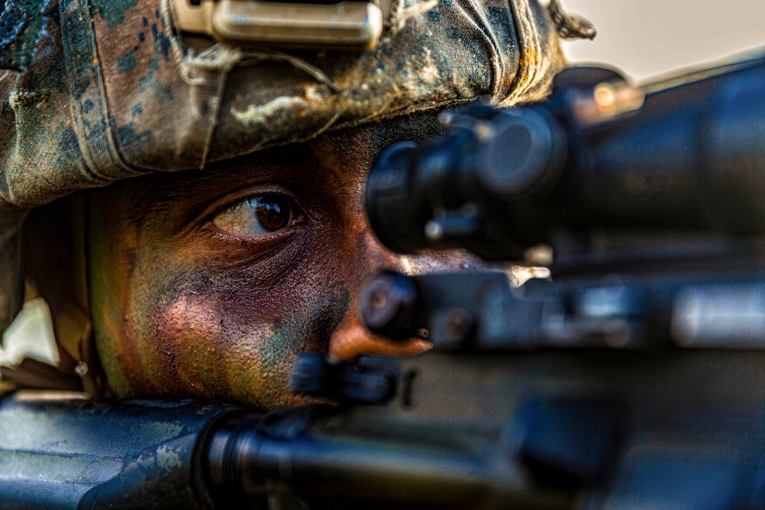 Close up of Marine in camouflage face paint looking through weapon scope.