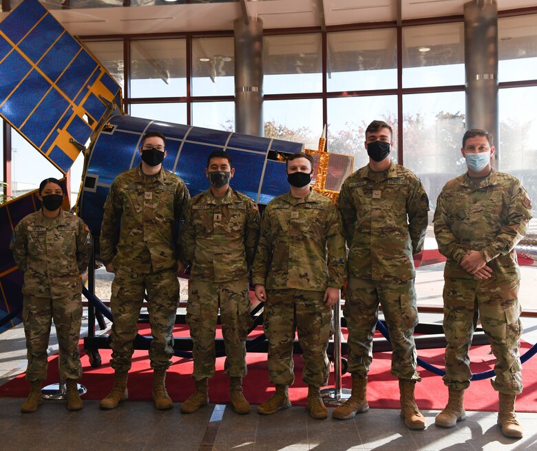 Military personnel posing for a photo in front of a satellite replica