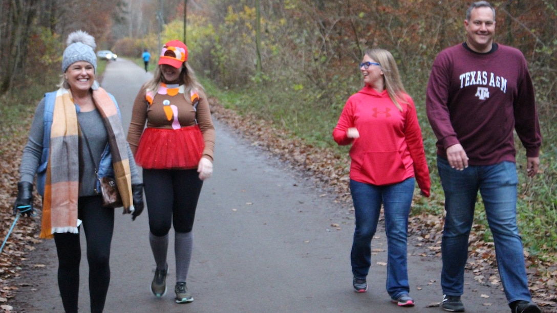 Four people walk and talk along a wooded path.