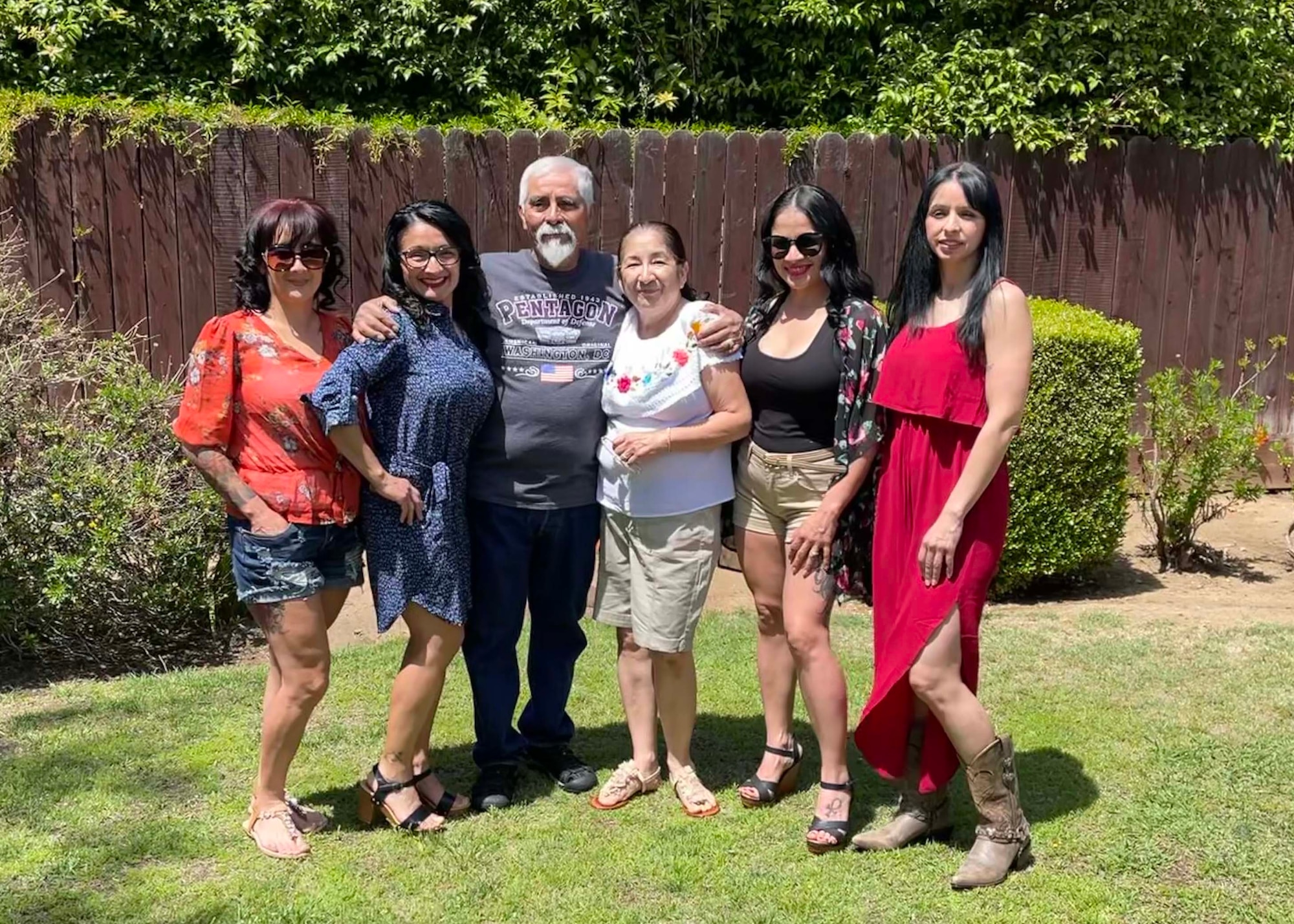 A family of six adults stand in their backyard to pose and take a group photo.