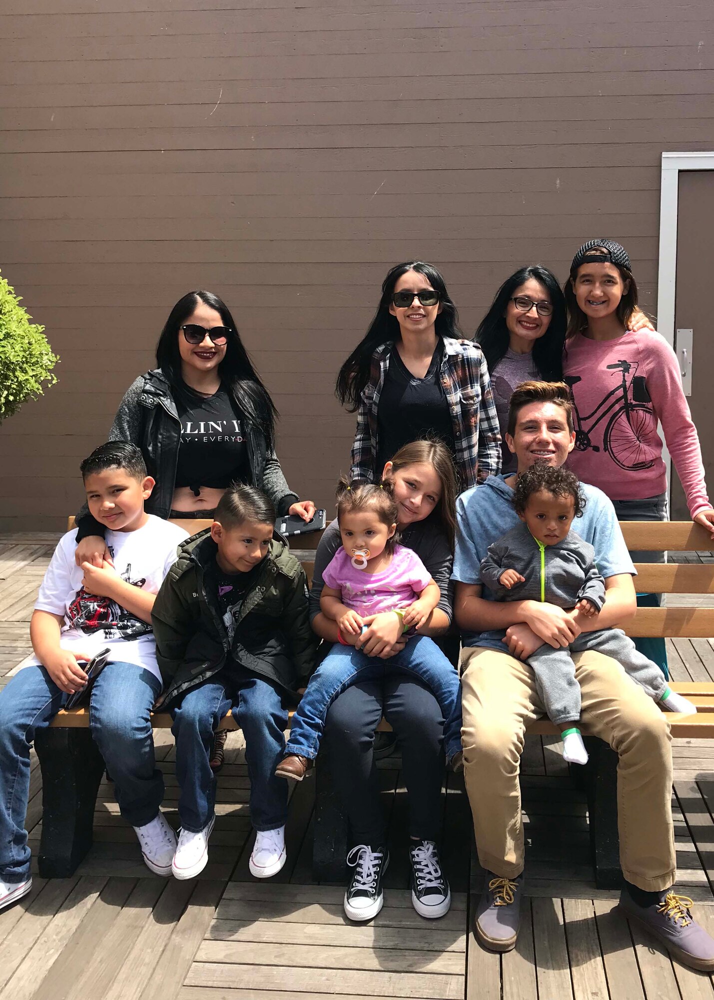 A group of three women and their seven children gather around and sit on a bench to pose for a group photo.