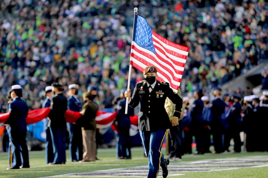 A soldier runs across a field holding an American flag.