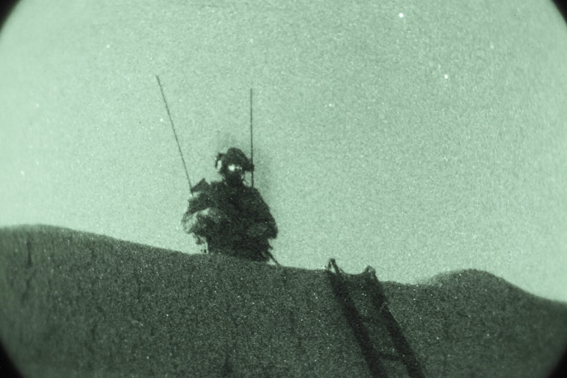 As seen through night-vision equipment, a soldier stands atop a building.