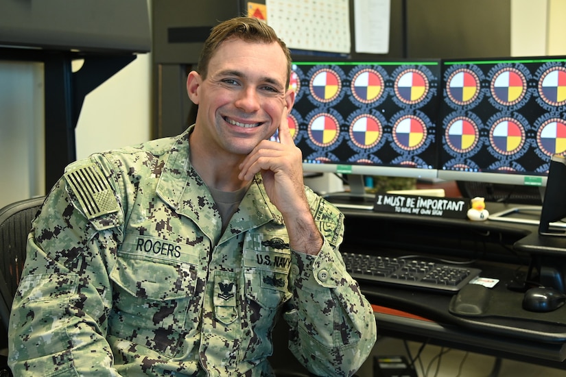 A sailor smiles while sitting at a desk.