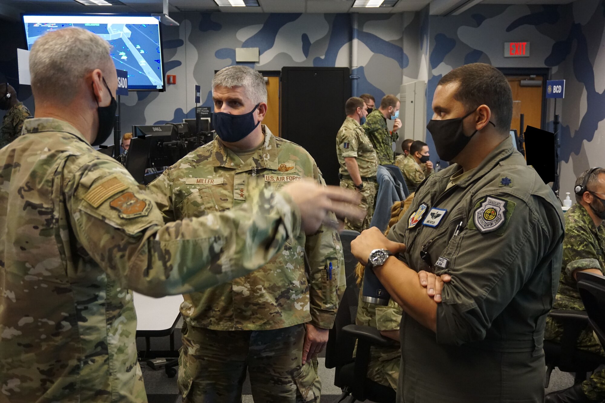 photo of U.S. Airmen briefing DV while coalition forces work on computers in background