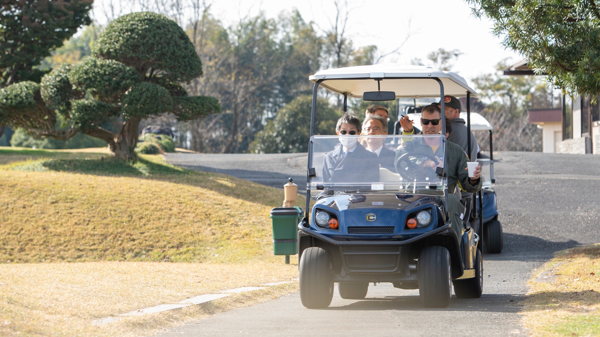 A group of Japanese and U.S. Air Force officials ride through a golf course on golf carts.