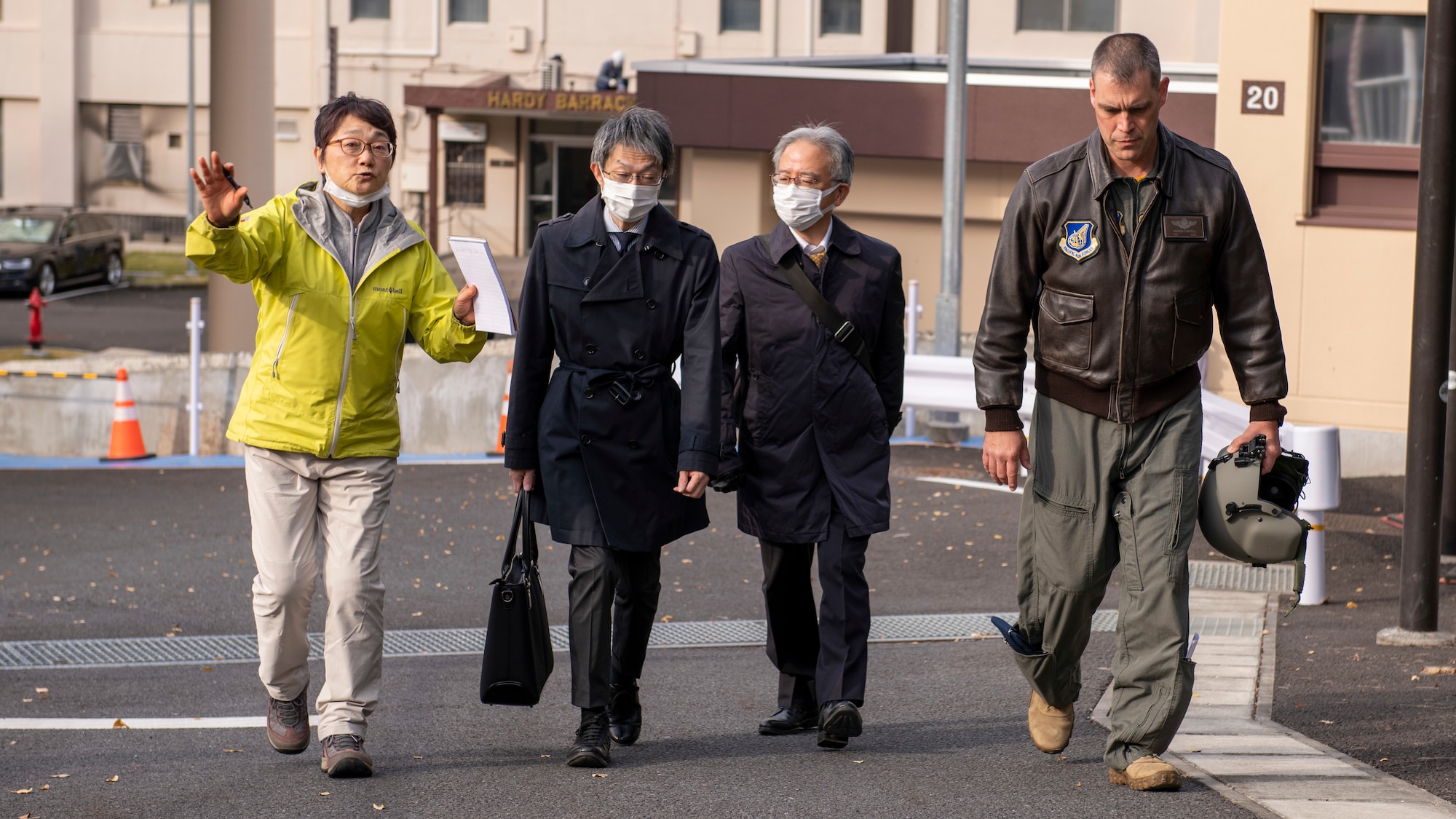 A Japanese translator in a yellow coat walks and talks with two Japanese government officials and a U.S. Air Force colonel in a flight suit.