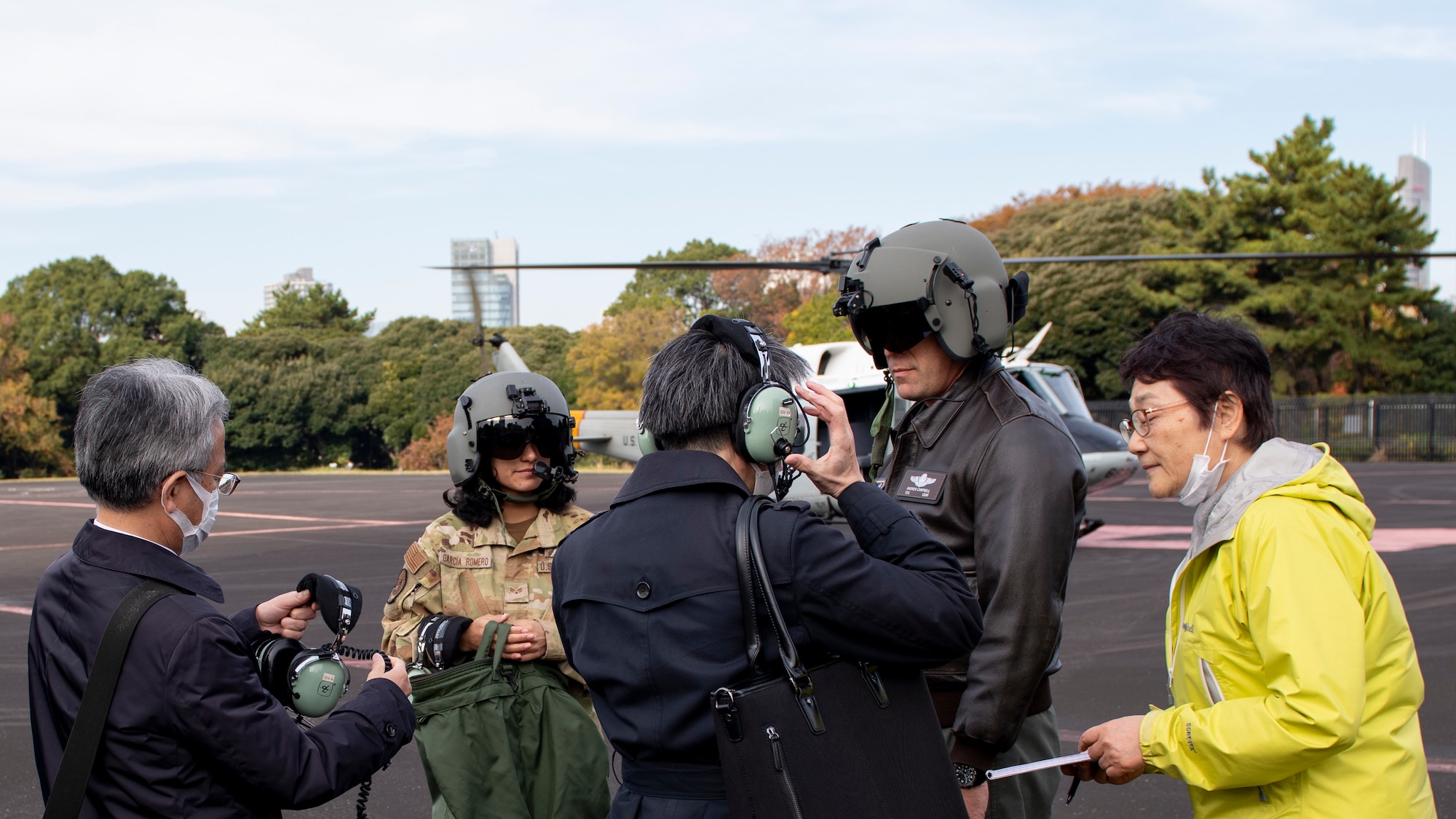 Two Japanese government officials don headsets with three U.S. Air Force Airmen, in front of a helicopter.