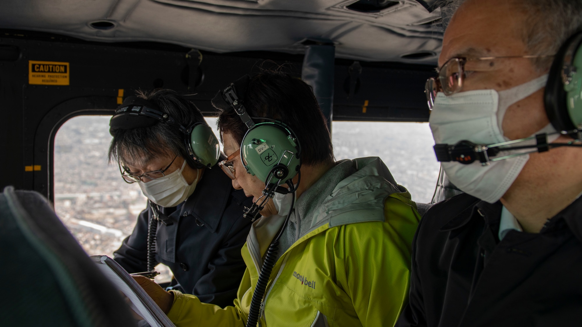 Three Japanese officials ride in the back of a helicopter.