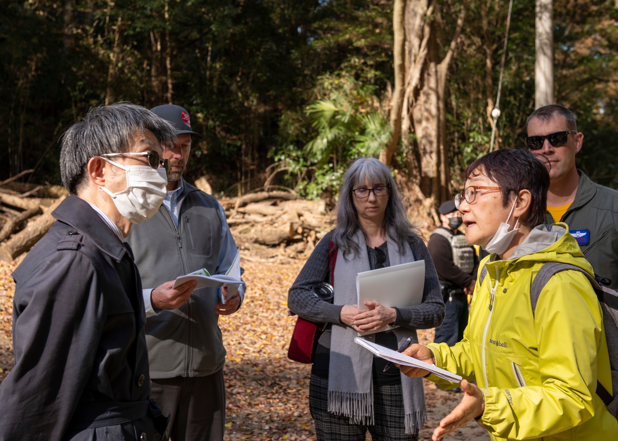 A female Japanese translator speaks to a local Japanese Government official in a wooded area.