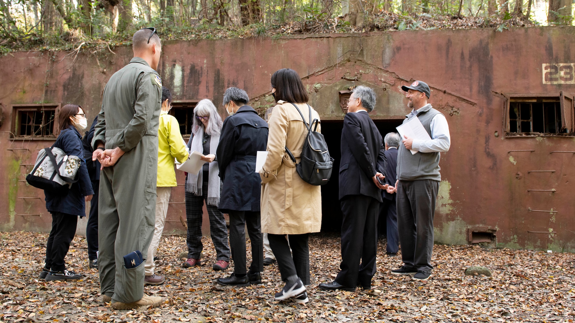 A group of U.S. Air Force and Japanese officials stand in front of a rusting WWII era ammo storage warehouse.