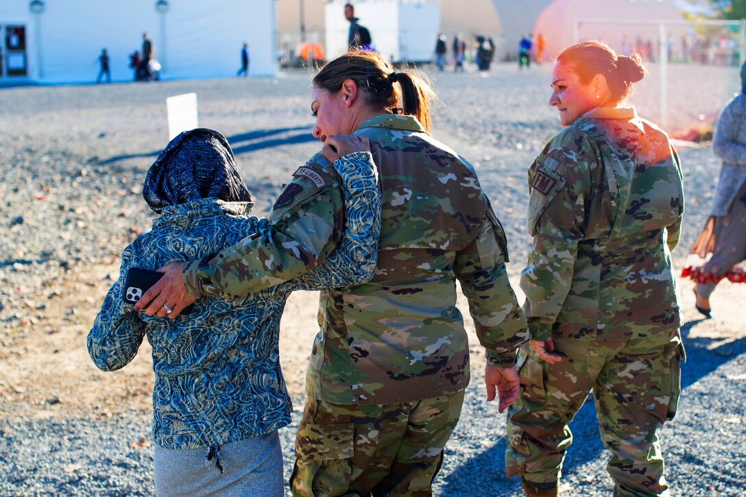 A female airmen puts her arm on the shoulders of an Afghan child while another airman walks with them.