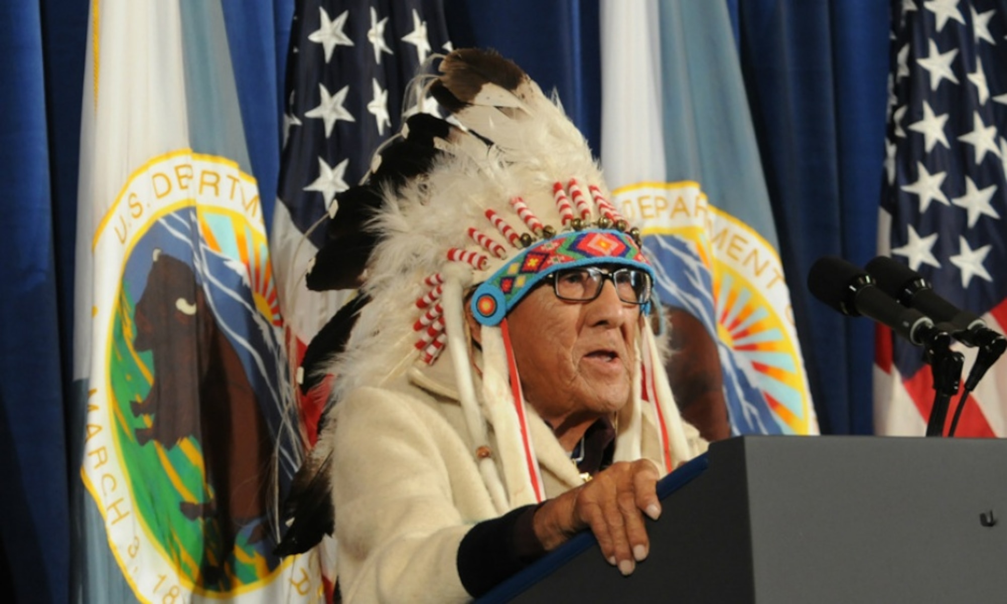 Dr. Joseph Medicine Crow gets on a stand and speaks.