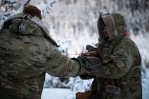 A U.S. Air Force Arctic Survival Training student hands a pile of firewood to a Survival, Evasion, Resistance and Escape specialist assigned to the Arctic Survival Training School during a recovery exercise on Eielson Air Force Base, Alaska, Nov. 18, 2021.