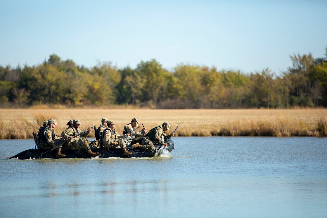 Army cadets use oars while riding in a rubber boat in a body of water.