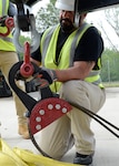 A man in safety vest and hard hat works with a heavy cable and hook as part of a rigging system.