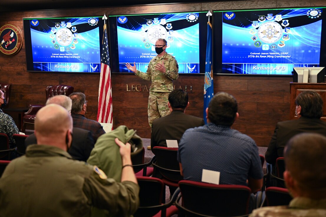 Military leader briefing a crowd in front of tv monitors
