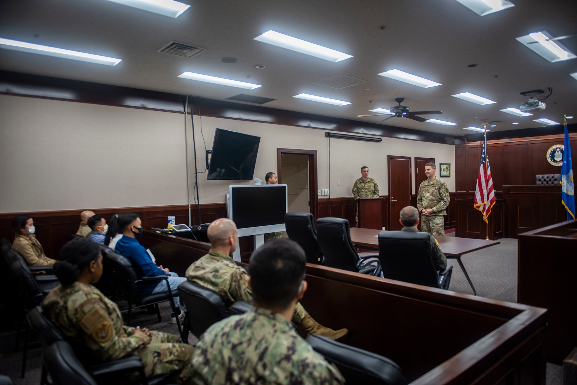 Military members in uniform sit in a courtroom.