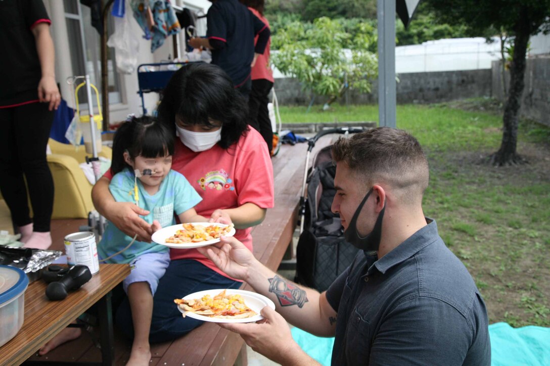 海兵隊員にピザとフライドポテトを差し出す女児、2021年11月22日、沖縄県西原町