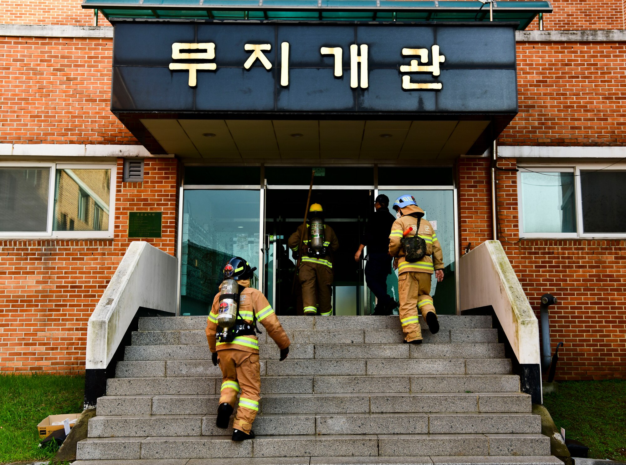 Airmen from the 8th Civil Engineer Squadron and 38th CES firefighter rush into building during a simulated structure fire at Kunsan Air Base, Republic of Korea, Nov. 4, 2021. Both 8th Fighter Wing and 38th Fighter Group firefighters were tested in their ability to respond quickly to a simulated structural fire on base. (U.S. Air Force photo by Staff Sgt. Jesenia Landaverde)