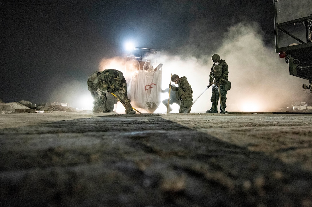 Airmen work at night  to repair a hole in the ground.