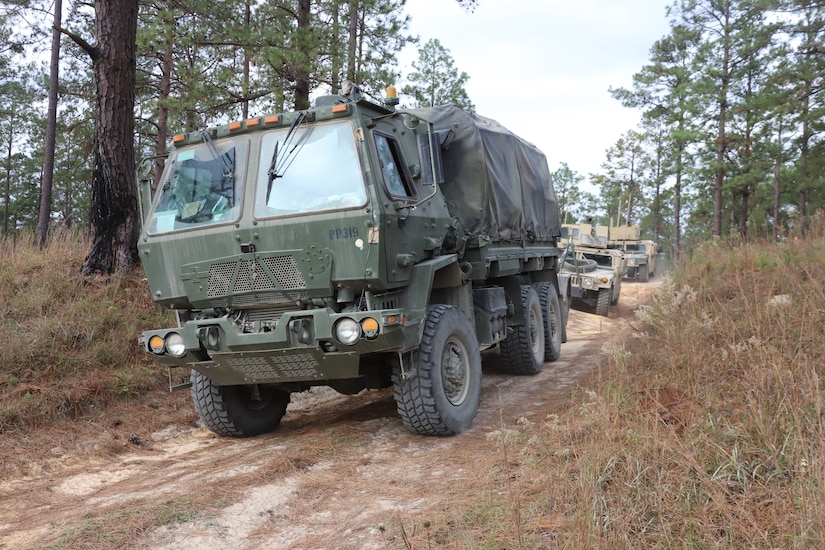 Trucks move down a dirt road.