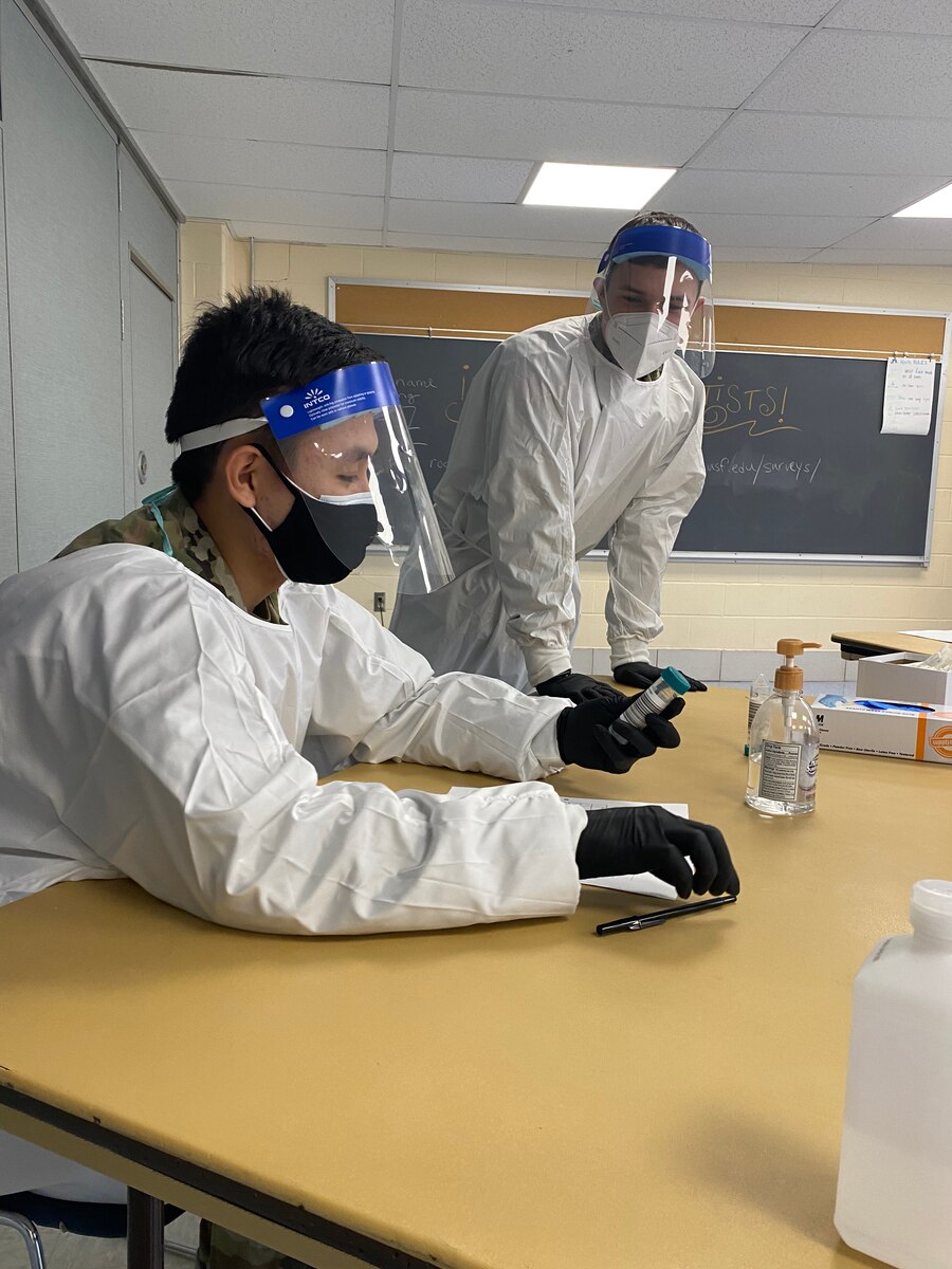 Airman 1st Class Tenzin Dakar, an aerospace medical technician with the 104th Medical Group, and Spc. Michael Major, a unit supply specialist with the 125th Quartermaster Company, examine a pool testing tube before conducting COVID-19 testing Nov. 17, 2021, in the Northampton, Massachusetts, school district. The Massachusetts National Guard was activated in mid-October to augment COVID-19 testing personnel in school districts across Massachusetts.