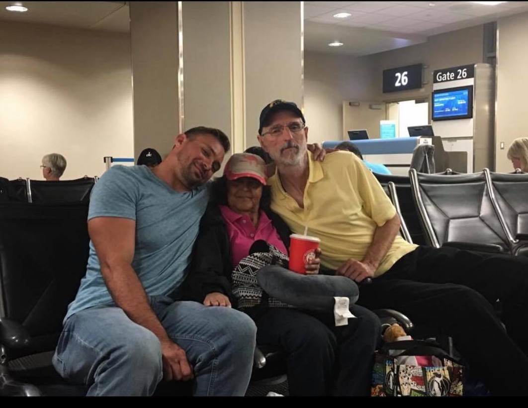 Three seated people pose for a photo near an airport gate.