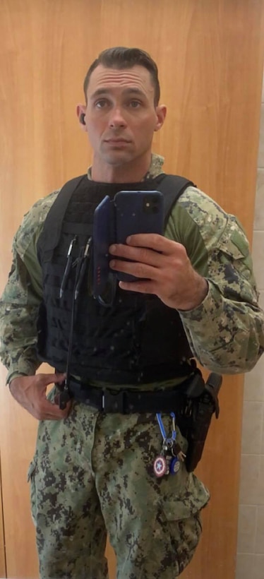 A sailor stands holding a phone.