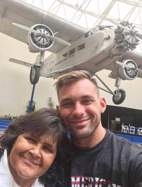 Two people pose for a photo with an aircraft image in the background.