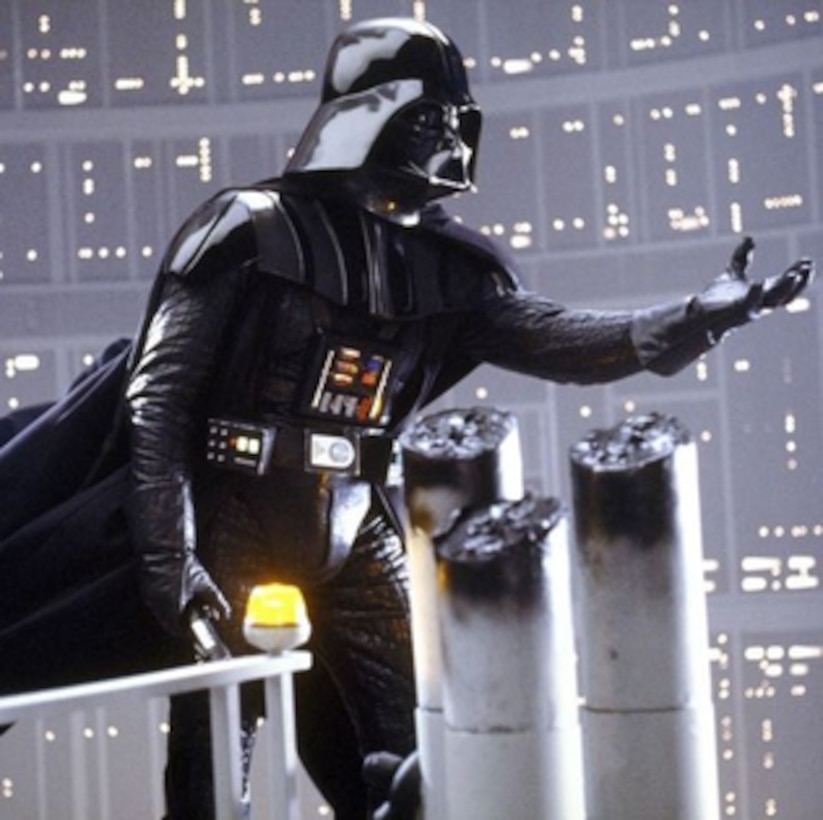 An actor in a Darth Vader costume reaches his hand out during a scene.
