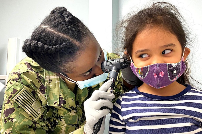 A sailor uses a medical device to look inside a girl's ear.