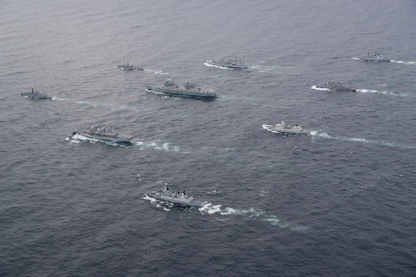 Multiple military ships move together in the ocean.