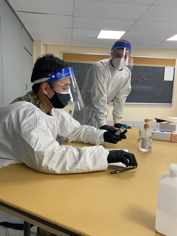 Airman 1st Class Tenzin Dakar, an aerospace medical technician with the 104th Medical Group, and Spc. Michael Major, a unit supply specialist with the 125 Quarter Master Company, overlook a pool testing tube prior to conducting COVID-19 testing Nov. 17, 2021, in the Northampton, Massachusetts, school district. The Massachusetts National Guard was activated in mid-October to augment COVID-19 testing personnel in school districts across the state.(U.S. Air National Guard photo by Staff Sgt. Hanna Smith)